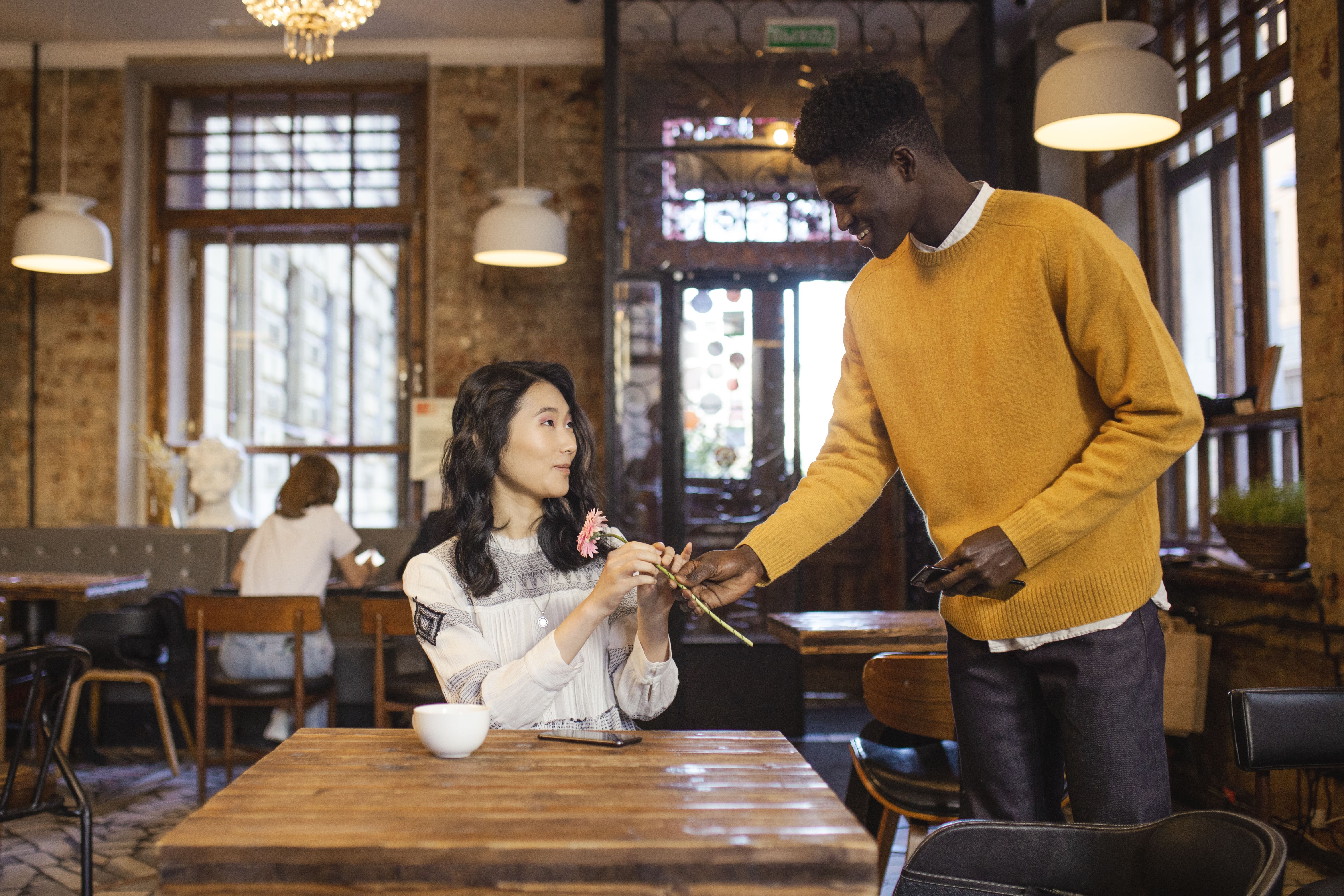 Man giving a flower to a woman during a date in a cozy café.