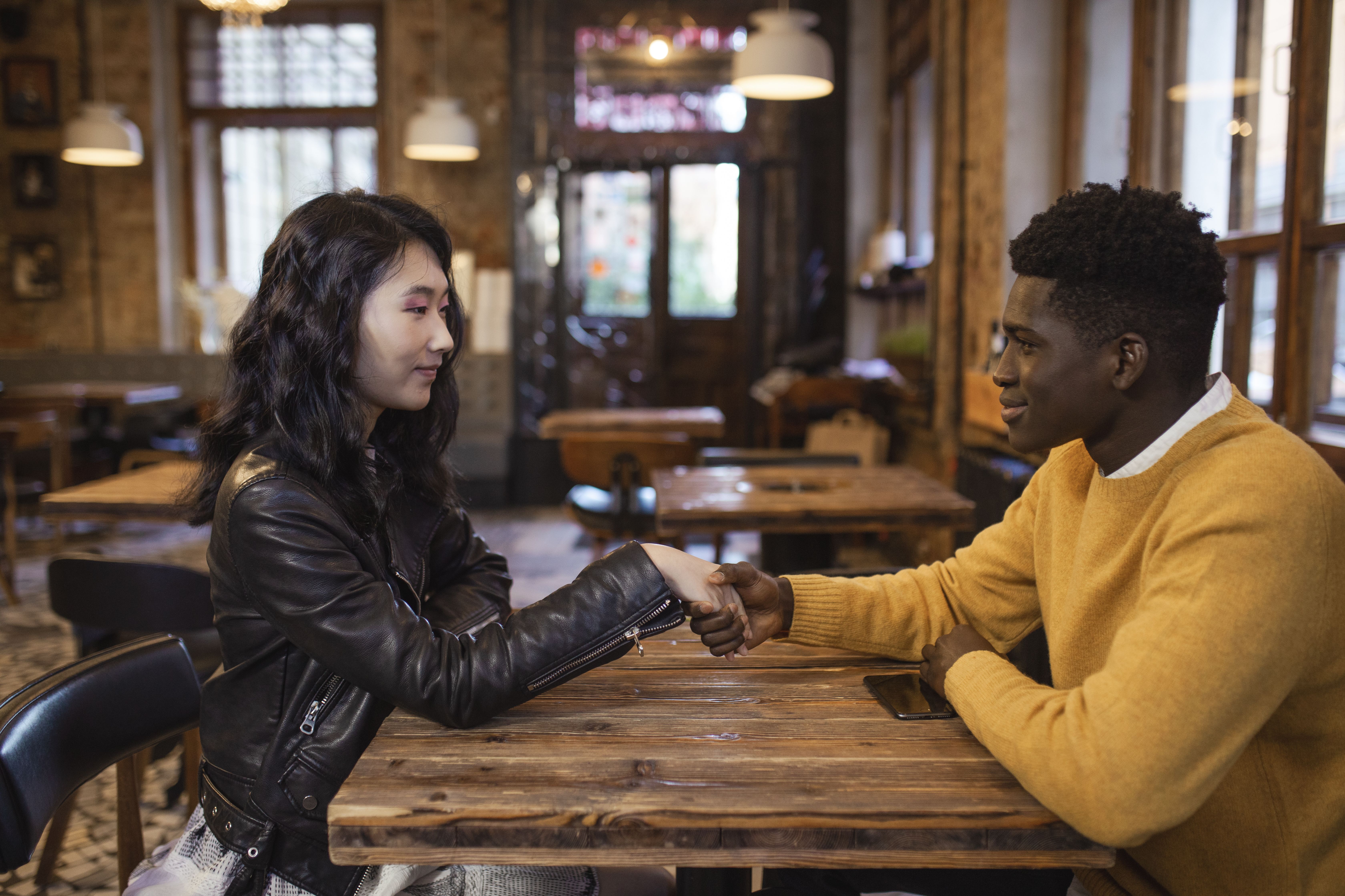 Diverse man and woman meeting in a café, shaking hands and smiling warmly.