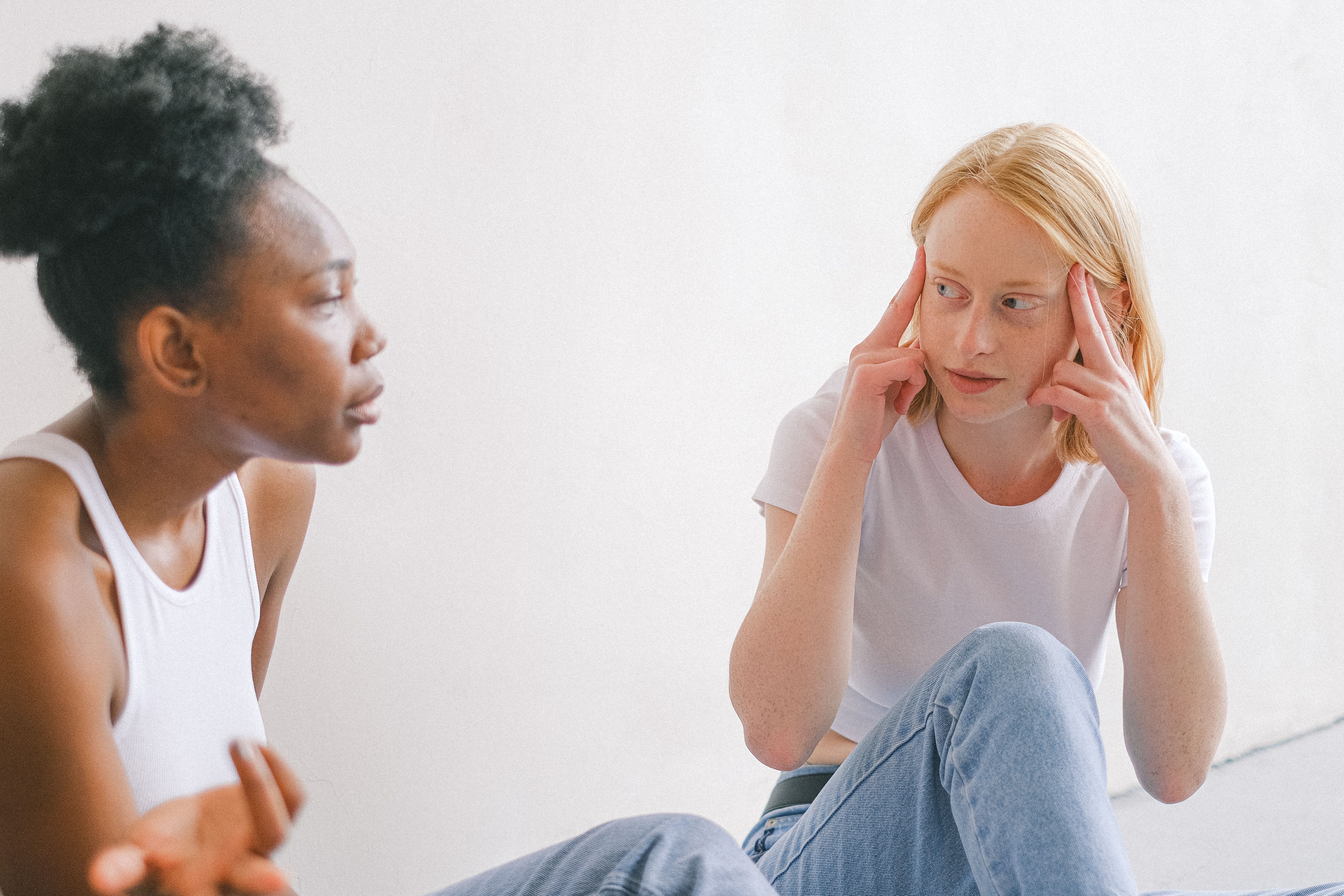 Two women in casual attire having an intense, friendly conversation indoors.